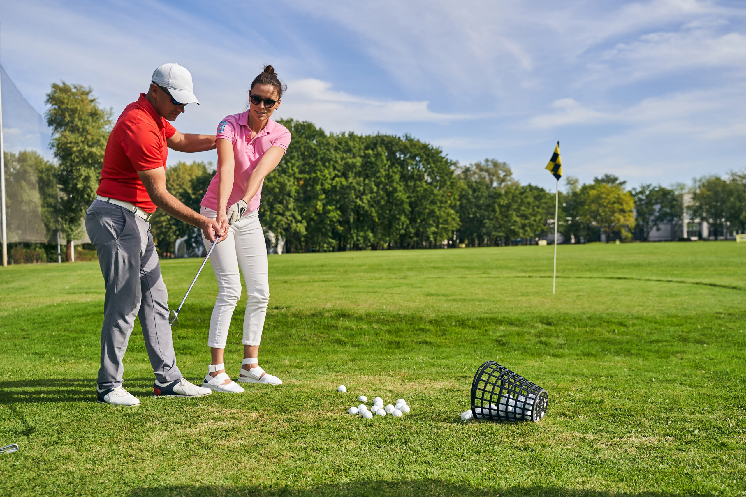 Young female athlete practicing a golf swing on the course helped by a skilled instructor